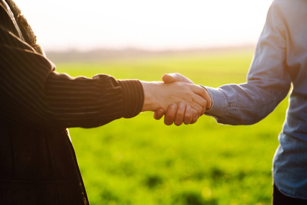 two people shaking hands on a grassy backdrop